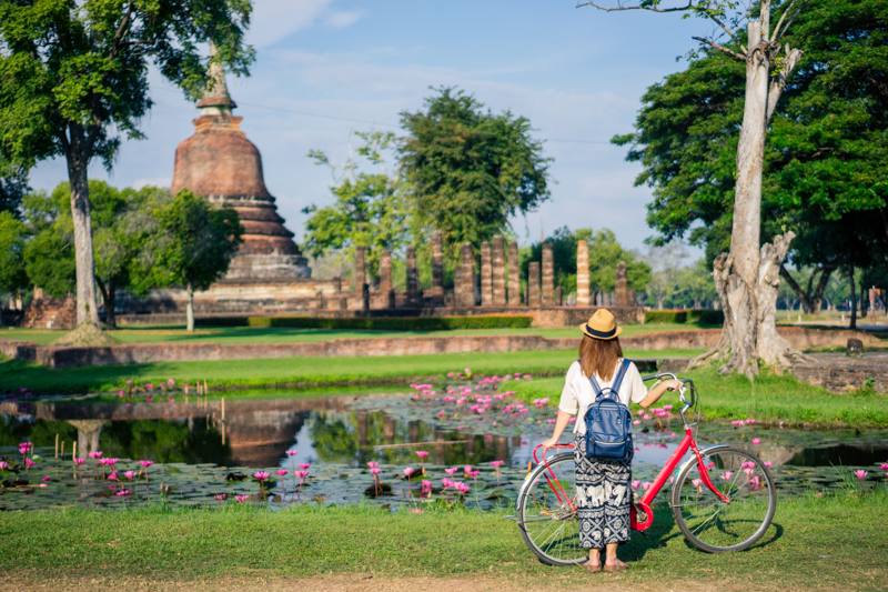 giovane donna che viaggia in bicicletta nel tempio di Wat Mahathat nel parco storico di Sukhothai contiene le rovine di vecchio Sukhothai, Thailandia,
